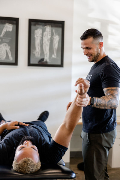 A chiropractor in St. George, Utah performs a shoulder mobility assessment on a patient lying on a treatment table.